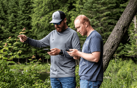 Pair of Paul Smith's students looking at their phones while on a walk in the woods